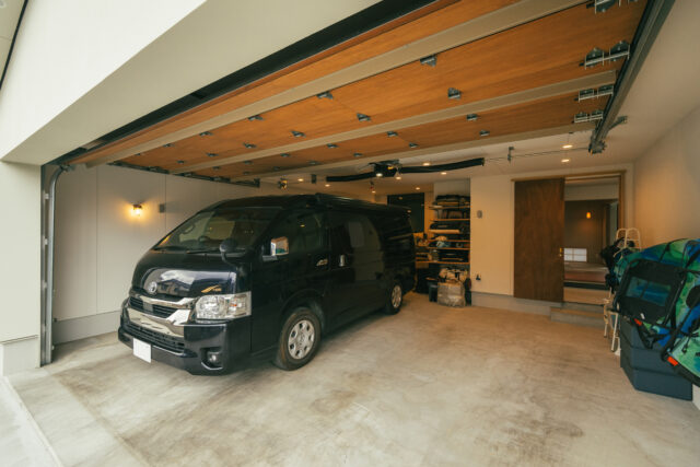 木製シャッター付きの屋内ガレージ。土間スペースに直接行くことができる（右）。キャンピングカーやキャンプ用品も収納でき、お施主様の趣味の部屋（左）からガラス越しに車を見ることもできる