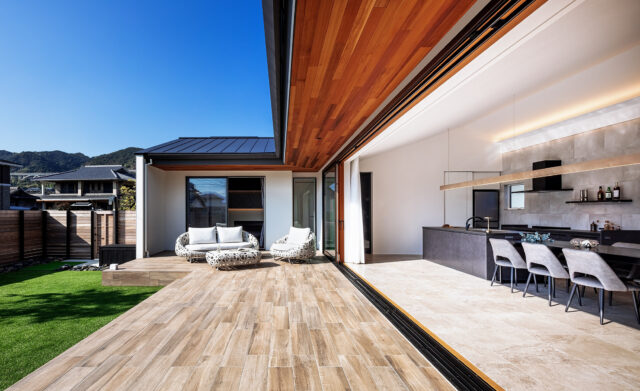 L字のテラスからLDKや庭を見渡す。正面は主寝室。テラスに張り出した庇は季節ごとの太陽高度を計算したうえで深さを計画。LDKも主寝室も一年を通して過ごしやすい。テラスは木目調パネル、LDKの床はタイルを取り入れたおかげで掃除しやすく、庭との行き来が気軽になった