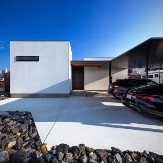 幹線道路側、西面の外観。中央の扉は玄関。左の白い箱はゲストルーム。ゲストルームの裏には小さな中庭を計画、家の内部に光を届けている。中庭をつくる余白を生む表現ができるのも平屋ならではの利点のひとつ、と石さん。庭に面した南側とは建物の見え方が異なるのもおもしろい