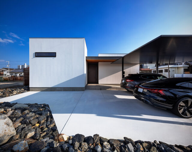 幹線道路側、西面の外観。中央の扉は玄関。左の白い箱はゲストルーム。ゲストルームの裏には小さな中庭を計画、家の内部に光を届けている。中庭をつくる余白を生む表現ができるのも平屋ならではの利点のひとつ、と石さん。庭に面した南側とは建物の見え方が異なるのもおもしろい