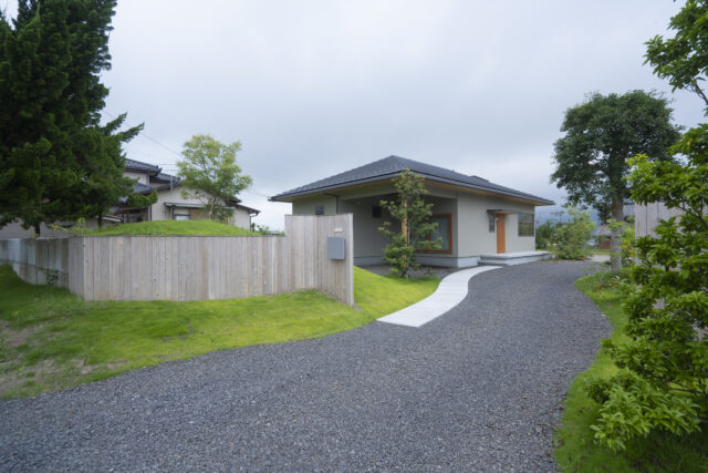 道路側から見た外観。建物の一角を屋根付きのテラスのような、用途を決めない空間として計画した。大きな洗濯物干しなど、便利使用されている。小高い丘の途中に外構が埋まっているよう。見た目も楽しい丘は高さ1.5ｍ程度あり、目隠しとしての役目を果たしている