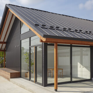 大屋根の軒天は垂木が見える現し仕上げで、木のぬくもりを感じさせる。街道側の一角は木工職人の息子さんが仕事で使うショールームとしてつくったスペース。ガラス張りのオープンでモダンなデザインが人目を引く