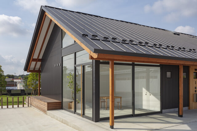 大屋根の軒天は垂木が見える現し仕上げで、木のぬくもりを感じさせる。街道側の一角は木工職人の息子さんが仕事で使うショールームとしてつくったスペース。ガラス張りのオープンでモダンなデザインが人目を引く
