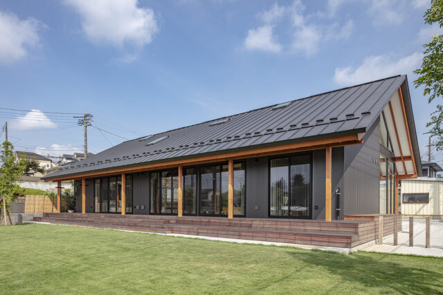 南の外観。柱は意匠としての化粧柱も入れて列柱をデザイン。高原のリゾートヴィラを彷彿とさせる高級感が生まれ、鮮やかな緑の庭とも好相性。連続する柱はウッドデッキののびやかな奥行きを強調する効果もある