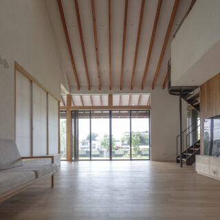 リビング。まっすぐのびた長い垂木が天井や庭に意識を向かわせ、開放感を強調する。内装は息子さんがつくった無垢材のテレビボードとのバランスを考慮し、床はナラ、天井や壁は珪藻土と漆喰のブレンドの左官塗り。木製の壁はパネルよりも厚みがあり素材感が生きるフローリング材