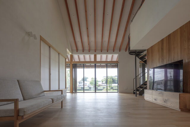 リビング。まっすぐのびた長い垂木が天井や庭に意識を向かわせ、開放感を強調する。内装は息子さんがつくった無垢材のテレビボードとのバランスを考慮し、床はナラ、天井や壁は珪藻土と漆喰のブレンドの左官塗り。木製の壁はパネルよりも厚みがあり素材感が生きるフローリング材
