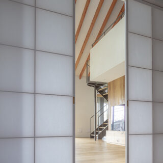 玄関ホールの先はリビング。障子戸の四角いマス、階段の曲線、垂木の斜線がグラフィカルな風景を生み出す
