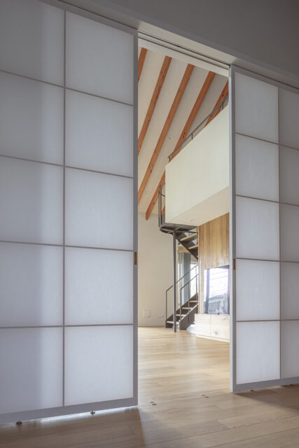 玄関ホールの先はリビング。障子戸の四角いマス、階段の曲線、垂木の斜線がグラフィカルな風景を生み出す