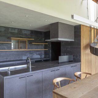 ダークグレーのキッチンの背面には、色のトーンを合わせた棚を設置。壁越しの廊下に面した小窓は風の通り道。要望の1つだった神棚は小窓の上に設置し、インテリアに溶け込ませている