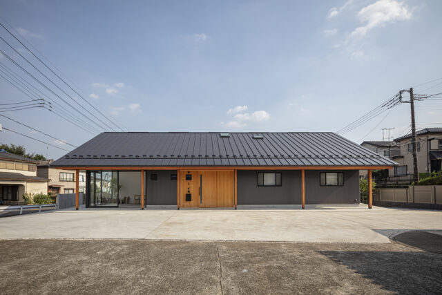 北の外観。手前のコンクリート広場は親族が集まる屋外の社交場。矢島さんがデザインした木製の玄関ドアは周囲の壁も板張りにして仕上げ、ガルバリウムの外壁とのバランスを取った。軒の木柱もアクセントとして生きていて、新年の門松なども似合う和モダンな佇まいになっている
