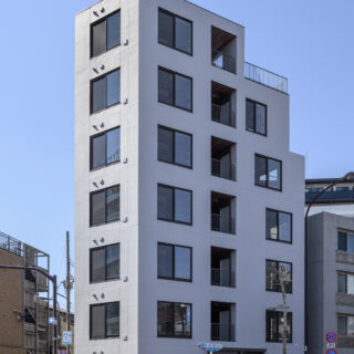 目白通り沿いのY字路のホームベース型の土地に建つFABRIC東長崎。周囲の街並みに溶け込むグレーを採用。同じサイズの窓が規則正しく連続し、バルコニーの突出もないため、スッキリした印象だ。