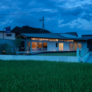 庭側外観夕景。室内から漏れ出る光が美しい。夜間でも境界壁のおかげで、外部からの視線を気にせず過ごすことができる。蛍の季節には、窓から庭の木にいる蛍を眺められるそうだ。妻は「毎年、とても神秘的で贅沢な時間を感じることができて満足です」と語ってくれた
