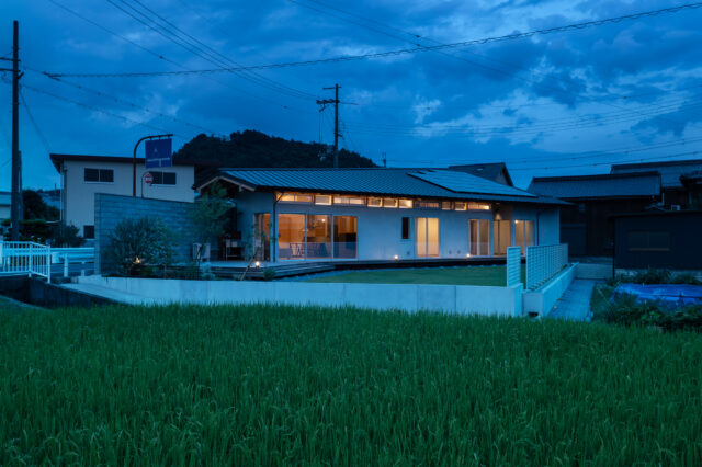 庭側外観夕景。室内から漏れ出る光が美しい。夜間でも境界壁のおかげで、外部からの視線を気にせず過ごすことができる。蛍の季節には、窓から庭の木にいる蛍を眺められるそうだ。妻は「毎年、とても神秘的で贅沢な時間を感じることができて満足です」と語ってくれた