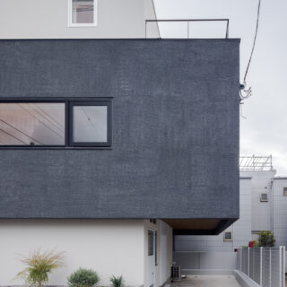 リビングのある２階部分を強調するため、白い箱にグレーの箱が一部重なるような構成とした。これにより、駐車スペースに軒がかかり、雨に濡れずに乗り降りできるように。