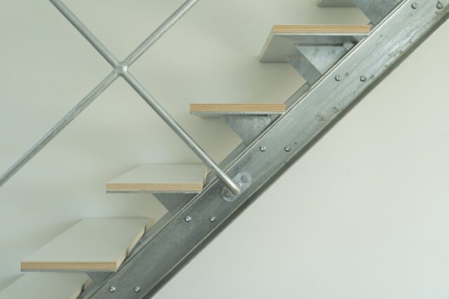階段は、無骨なイメージを表現するため、また印象がシンプルになりすぎないよう、デザインの足し算を施した。ビスは強度的には必要ないが、鉄の質感をより強く押し出すためにつけた。踏板のシナ合板は表面を白く塗装し、側面の共芯の表情は楽しめるようにした