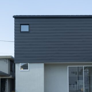 南からみた外観。旗竿地の最奥にあるため、道路から見えやすい2階が目立つように計画。1階のサッシの高さと、2階外壁のガルバリウム鋼板の高さを揃え、外観のラインもシンプルに整えた。家の手前は中庭。左隣の建物は親族の家。庭を共有し、行き来できるよう家を配置した