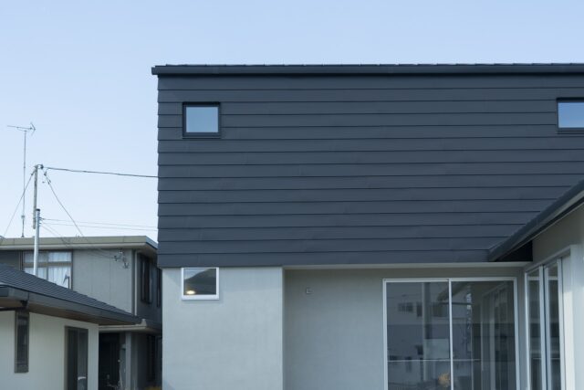 南からみた外観。旗竿地の最奥にあるため、道路から見えやすい2階が目立つように計画。1階のサッシの高さと、2階外壁のガルバリウム鋼板の高さを揃え、外観のラインもシンプルに整えた。家の手前は中庭。左隣の建物は親族の家。庭を共有し、行き来できるよう家を配置した