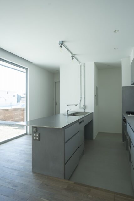 1階キッチン。冷蔵庫は生活感が出ないよう右奥のパントリーに設置する。左奥の仕切り戸は水回りへ続く