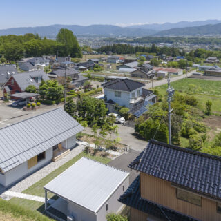 伊那市内の高台に佇む「西春近の家」（写真左下）。遠く東に南アルプスを望む眺望に恵まれた立地は大きな魅力。外観デザインはシンプルかつナチュラルで、周囲の長閑な景色に溶け込んでいる