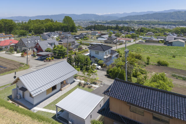 伊那市内の高台に佇む「西春近の家」（写真左下）。遠く東に南アルプスを望む眺望に恵まれた立地は大きな魅力。外観デザインはシンプルかつナチュラルで、周囲の長閑な景色に溶け込んでいる