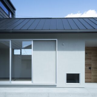 中庭から見た外観。右奥、木材の壁面の扉は書斎のもの。玄関扉は左壁面にある。「離れているほうが集中できるので」と一度外に出てアクセスする間取りを提案したと武本さん。中庭を行き来し、左のサッシ窓を介して妹さま家族とやりとりすることもあるのだとか