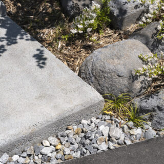 玄関へのアプローチの足元にも注目。天然石や木製チップにマッチするよう、コンクリートのステップはあえて磨かずざらりとした質感を残し、カドには丸みもつけた。「周囲の自然と調和させる」という酒井さんの意図を汲んだ造園屋さんの細やかなテクニックだ