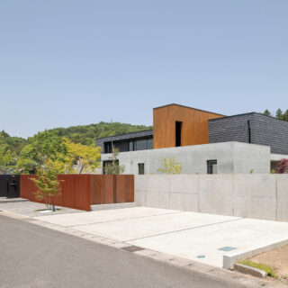 外観。来客用の駐車場を3台設けて外構を下げ、圧迫感を軽減。来客は黒い仕切りからアプローチへ進む。コンクリート壁と垂直に交わる茶色い壁の素材は錆びることで安定するコールテン鋼。その横の屏風の鉄板を取り外すことで、ご主人の庭づくりのための重機がここから搬入できる