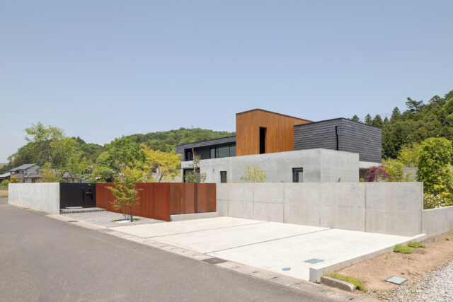 外観。来客用の駐車場を3台設けて外構を下げ、圧迫感を軽減。来客は黒い仕切りからアプローチへ進む。コンクリート壁と垂直に交わる茶色い壁の素材は錆びることで安定するコールテン鋼。その横の屏風の鉄板を取り外すことで、ご主人の庭づくりのための重機がここから搬入できる