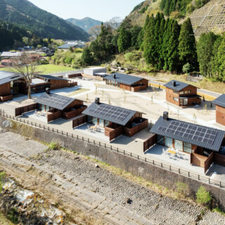 北側高所から見た全景。手前3棟並ぶのはA棟。下を流れる川の向こうには山がそびえている。川が流れ、さらに南からの光を受け止めた山の木々が美しいことから、リビングからテラスまでを一体化させて外に出やすくし、存分に楽しめるように整えた