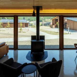 C棟、共用リビング。薪ストーブは他の宿泊者たちも行き交う庭側に大きく開口した窓の中央に設置。宿泊者同士で交流し、情報交換する場になって欲しいと計画したパブリックスペース。薪ストーブを囲んで談笑する様子を見て、他の棟の宿泊者も足を止めるかもしれない
