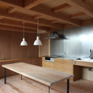 キッチン・ダイニング。家具やテーブルはすべて造作だ。キッチンの壁面は金属素材のZAM。高耐食性メッキ鋼板で磁石が使え、錆びにくい。デザイン面でのアクセントと掃除などのしやすさも採用の理由となった。鴨居に照明を組み込み、このスペースもシンプルに