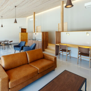 C棟、共用リビング。仕事ができるカウンターやくつろげるソファ、テーブルなど、状況や気分に合わせて居場所を選択できる。カウンターの奥は個室への扉が並ぶ。低めの壁を配置し、さらに段差を付けることで、個室とパブリックスペース間での意識の切り替えを促している
