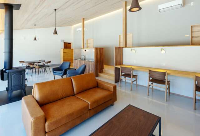 C棟、共用リビング。仕事ができるカウンターやくつろげるソファ、テーブルなど、状況や気分に合わせて居場所を選択できる。カウンターの奥は個室への扉が並ぶ。低めの壁を配置し、さらに段差を付けることで、個室とパブリックスペース間での意識の切り替えを促している
