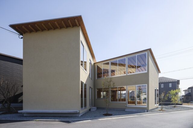 北西から見た外観。左端の木を残したいという要望から、北側に庭を計画。さらに西側に中庭も設けた。くの字の建物のうち、右側１階が機能訓練室。掃き出し窓からアクセスし、中庭をより豊かに活用できるように設えた。利用者様スタッフさんみんなで庭づくりを楽しまれている