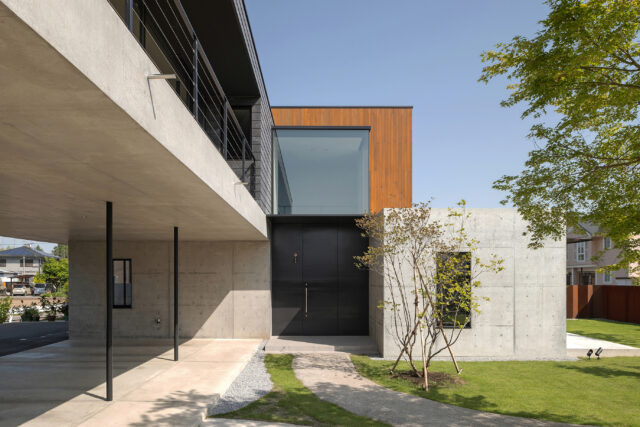 リビング前の庭、アプローチから玄関を見る。奥さまのご希望により玄関は約3.2ｍの鉄製のものを採用。玄関上にあるのが吹き抜けの開口。屋根を薄くするなど工夫し「ガラスの箱がついているように見せたかった」とのこと。画像左は駐車場。雨の日でも濡れずに室内に入れると好評だ