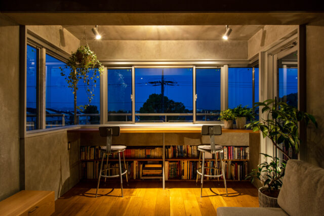 眺めのいい窓辺でクリエイティブな仕事ができたらと、リビングの一角に設えたカウンタースペース。カウンターテーブルの下に本棚を造作して使い勝手を高めた。三面採光で昼は明るく開放的、夜はスポットライトの灯りの下リラックスして過ごせる