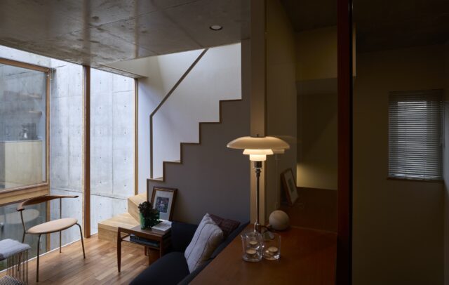 子世帯のリビングスペース（写真左）。コンパクトだが中庭に面しているので視線が通り、外光や上下の広がりを感じられる。中庭側は天井から床までガラスがはめ込まれて屋外との境界があいまいになり、室内なのにテラスにいるような居心地を味わえる