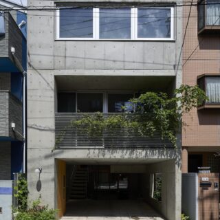 コンクリート打ち放しに木材や緑を組み合わせた上品な外観。道路沿いは駐車場で、その奥に半地下がある