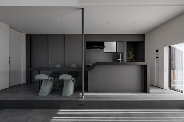 1階、3間×3間の正方形の中に配したLDK、リビングからキッチン、ダイニングを見る。アイランドキッチンは造作し、ダイニングテーブルと一体化させた。背面の棚には食器に加えて冷蔵庫を含む家電なども収納でき、生活感がない空間を実現。左壁面の仕切り戸は水回りに続く