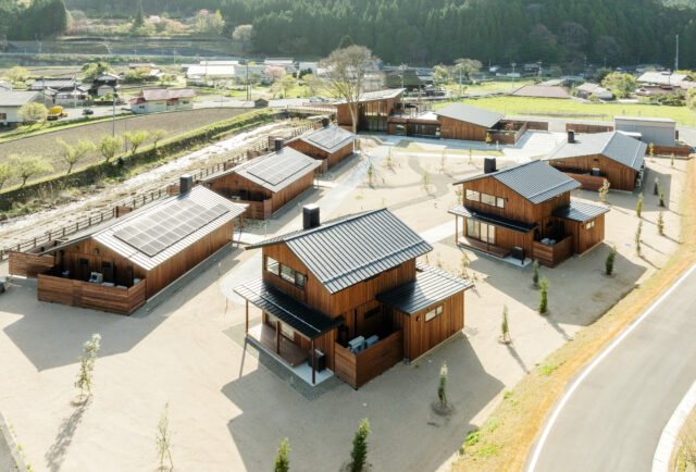 西側高所からの全景。左側に並ぶのはA棟、右に2つ並ぶ棟はB棟。収容人数は同じながら、大きな平屋のA棟に対して、B棟は高さを抑えたコンパクトな2階建て。B棟の2階からは、A棟からも見える美しい山が眺められる。場の持つイメージを踏まえ、宿泊施設は全て切妻屋根とした