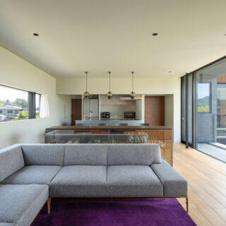 2階奥からキッチン、ダイニング、リビング。キッチンを挟み右の扉は廊下へ、左の扉はパントリーへ続く。キッチンは対面式。右の大開口は深い庇があり、夏の直射日光を遮る。また天井の中にロールスクリーンボックスを設え、普段はロールスクリーンが見えないよう設計されている