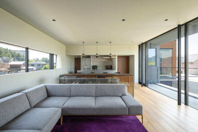 2階奥からキッチン、ダイニング、リビング。キッチンを挟み右の扉は廊下へ、左の扉はパントリーへ続く。キッチンは対面式。右の大開口は深い庇があり、夏の直射日光を遮る。また天井の中にロールスクリーンボックスを設え、普段はロールスクリーンが見えないよう設計されている