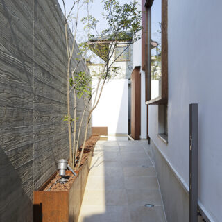 エントランスはあえて長いスロープを進むアプローチとした。道路からの目隠しも兼ねた浮きづくり塀には、杉の木目をつけ立体感を演出。品の良い飲食店を訪れたときのように路地を進むワクワク感が演出されている。
