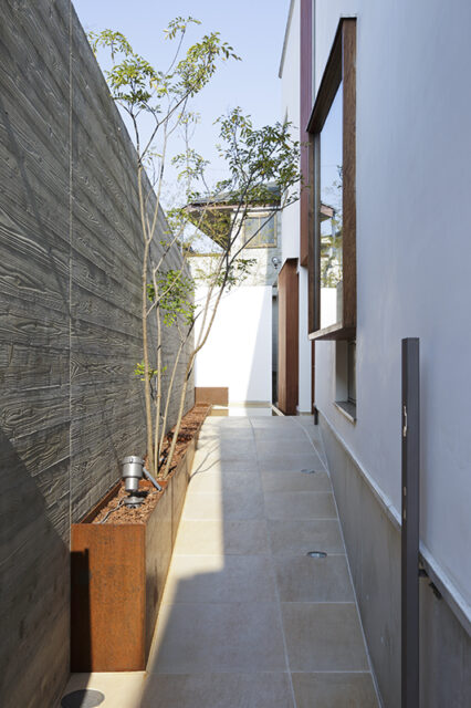 エントランスはあえて長いスロープを進むアプローチとした。道路からの目隠しも兼ねた浮きづくり塀には、杉の木目をつけ立体感を演出。品の良い飲食店を訪れたときのように路地を進むワクワク感が演出されている。
