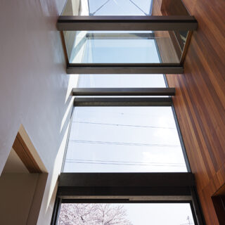 左右の２棟の建物がガラスでつながるエントランスホールは、２層吹き抜けで上部から光が降り注ぐ。視線の先の桜の木が、ようこそと出迎えてくれるかのよう。
