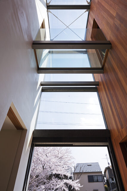 左右の２棟の建物がガラスでつながるエントランスホールは、２層吹き抜けで上部から光が降り注ぐ。視線の先の桜の木が、ようこそと出迎えてくれるかのよう。
