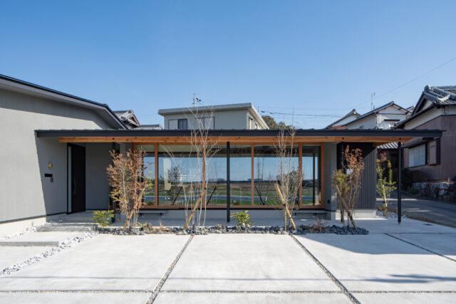 外観（西側正面）。景観が良い西側を大きく開き、そこにLDKを配した（写真中央）。L字型の平屋とし、写真左のエリアには寝室や水回り、子供部屋や収納スペースを集中的に配置。効率的な導線となるプランとした。平屋としたことで、背後の家からも田園風景を眺めることができる