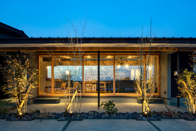 西側外観（夕景）。植栽を照らす照明と、室内から漏れ出る柔らかな光が美しい。この照明を含め、外構もセットで設計されている