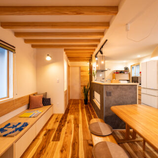 ヌック側からLDKを見通す。ご要望から壁際の下部に収納付きのベンチを造作した。以前の壁はクロス張りだったが、クロスの上から漆喰を塗り自然素材の空気感に満ちた空間を実現。そのうえでベンチには「漆喰に背中を付けるのもあまりよくないので」と木材の背もたれも設置した