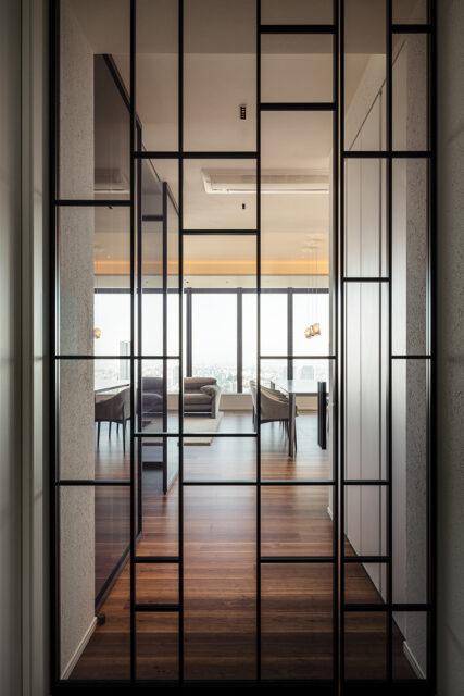 グリッド状の桟が印象的な扉。グレーのガラスが、窓先の景色まで見渡せる抜け感と、玄関が見えない実用性を両立。